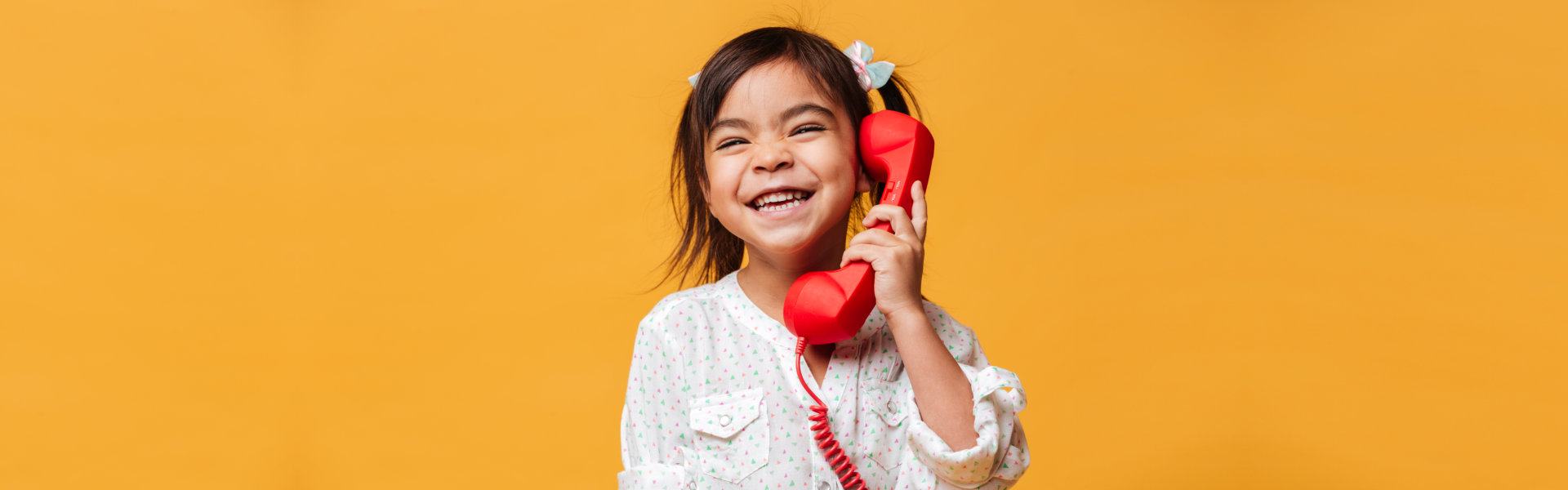 Happy excited little girl talking by red retro telephone